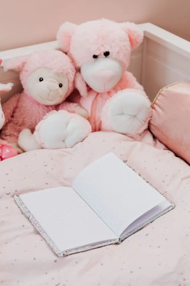 Pink plush toys beside an open notebook on a soft pink bed
